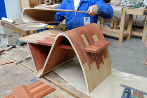 L'image montre un élève en train de réaliser un objet en bois sur un établi à l'atelier