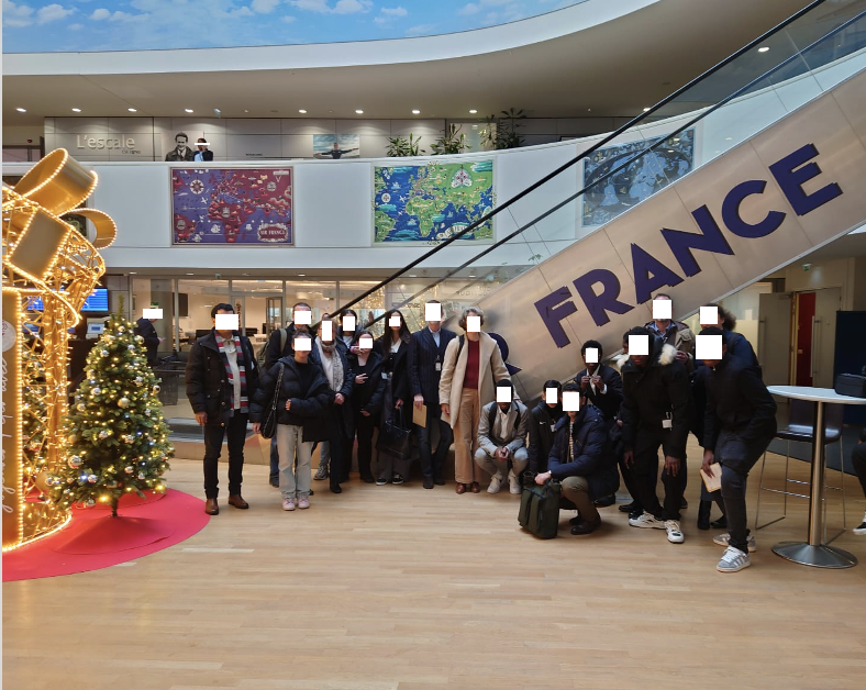 Cette image est une photo de groupe devant un Escalator où est inscrit (Air) France.