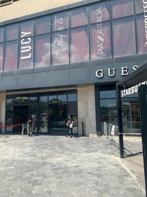 Cette image montre la vitrine du magasin Guess à l'entrée du centre commercial. La devanture est vitrée et donne sur une grande place carrelée grise