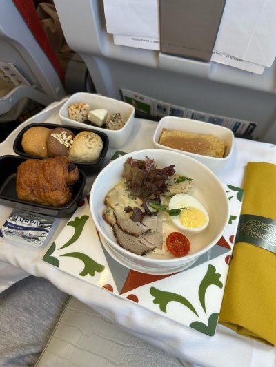 Cette image montre le repas servi dans l'avion : un pain, du frimas, un morceau de cake, des gâteau et une salade avec un oeuf