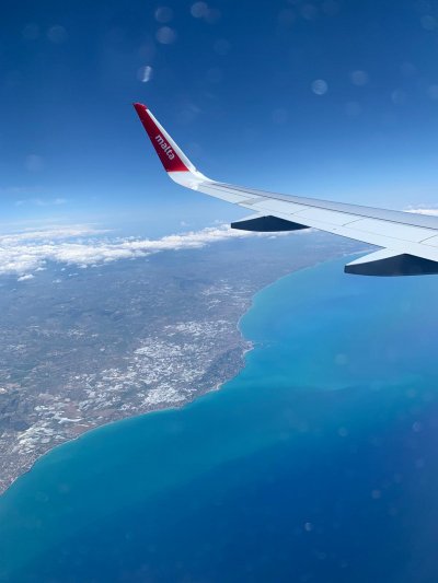 Cette image est une photo prise du hublot de l'agio et montre son aile au dessus de la mer et d'une côte terrestre