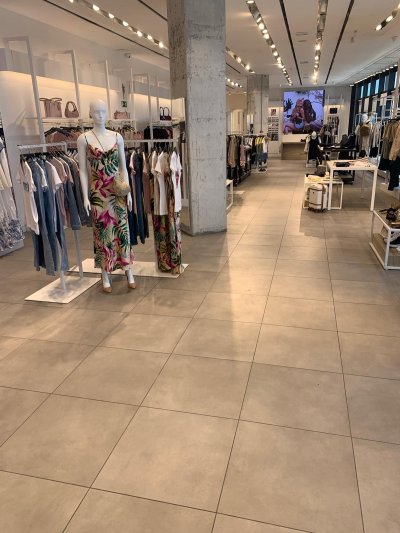 Cette image montre l'intérieur du magasin Guess : sol carrelé gris, rails de spots lumineux au plafond, rayonnages et mannequin