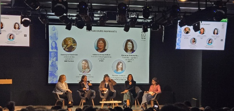Cette photo représente 5 professionnelles de la tech assises sur la scène de l'auditorium. Derrière elle un écran expose leurs visages et leurs noms.